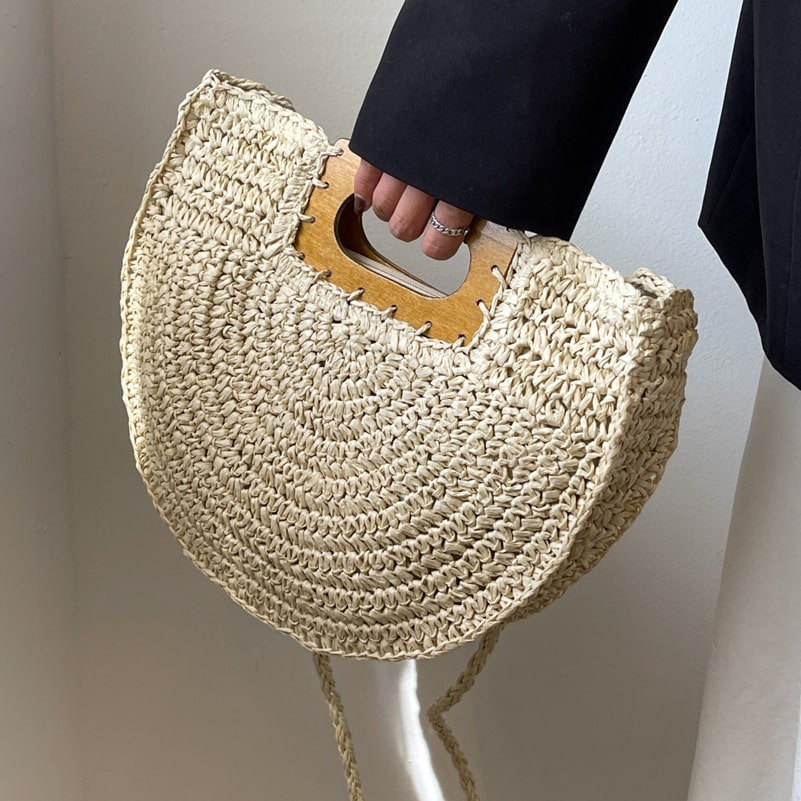 Rounded rattan handbag with a raw wood handle – worn by a model