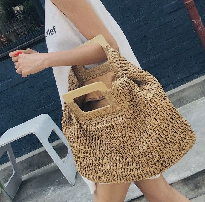Woven straw tote with varnished wooden handles – worn by a model