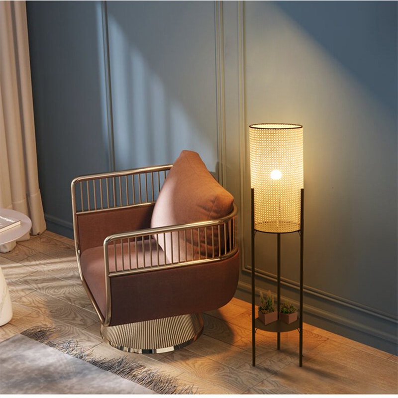Modern cylindrical rattan table lamp on a matte metal stand – shown lit in a room setting