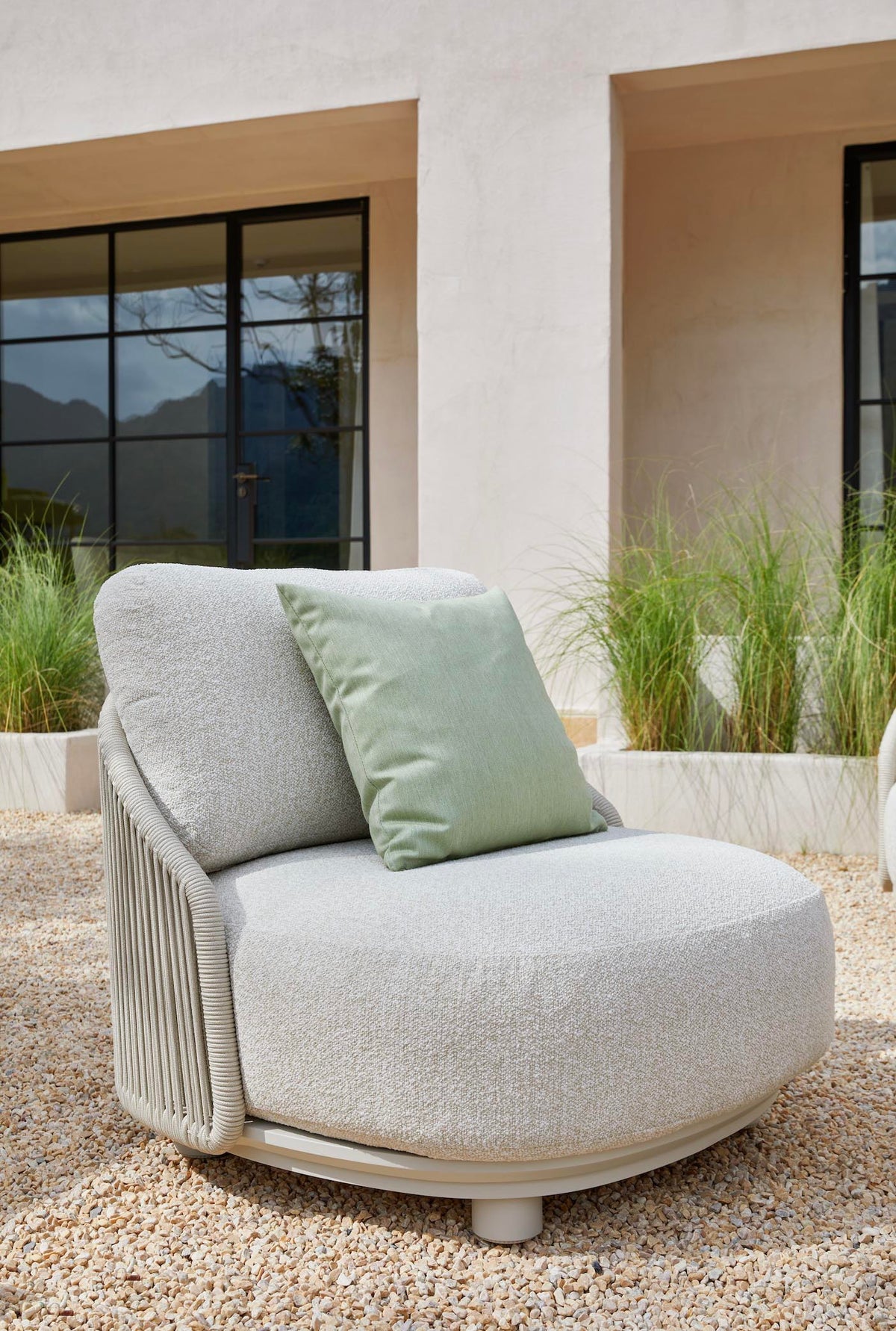 Armchair from the Aura beige rope outdoor lounge set with free-form ceramic coffee table – shown outdoors