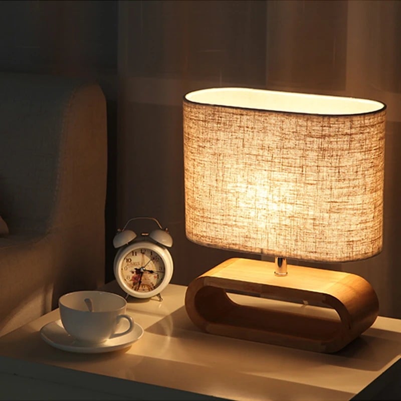 Rounded handwoven rattan bedside lamp in natural tones – shown lit in a room setting