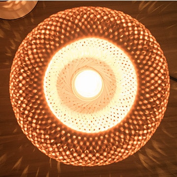 Round handwoven rattan table lamp on a metal base – close-up detail, lit