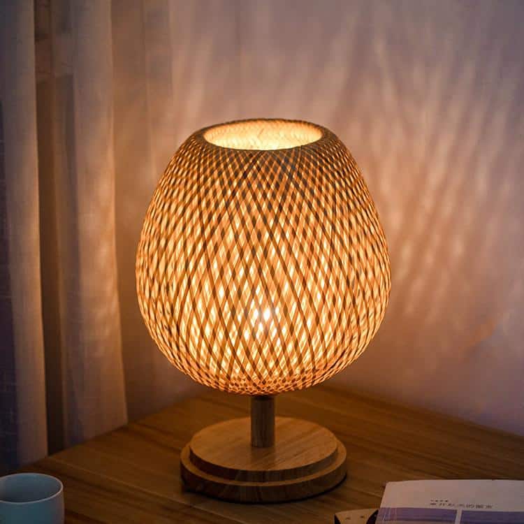 Round handwoven rattan bedside lamp on a solid wood base – shown lit in a room setting