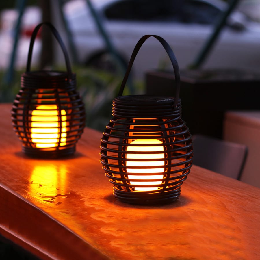 Hanging handwoven solar rattan lantern with an integrated handle – shown lit outdoors