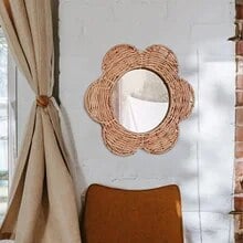 Natural rattan flower wall mirror with braided petals and a circular center – shown in a room setting (2)