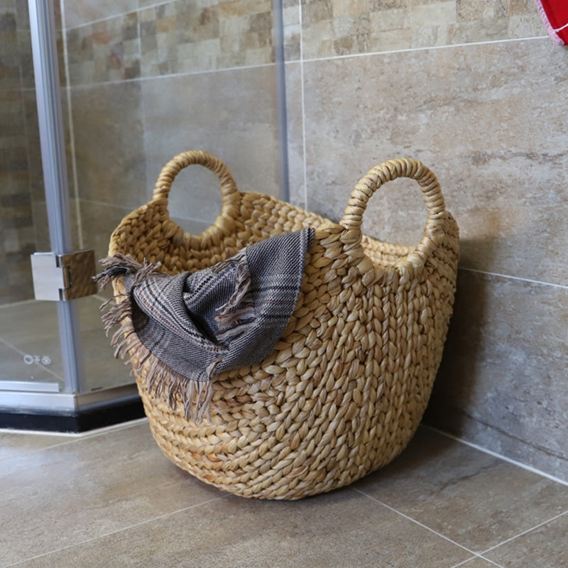 Natural rattan laundry basket with two side handles – shown in a room setting (3)