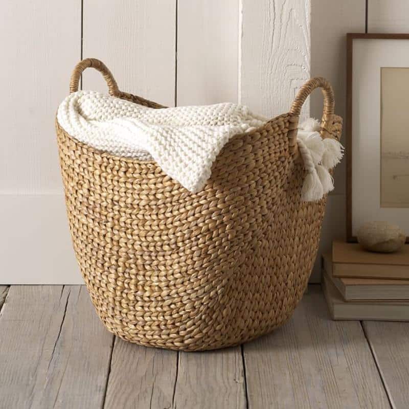 Natural rattan laundry basket with two side handles – shown in a room setting (2)