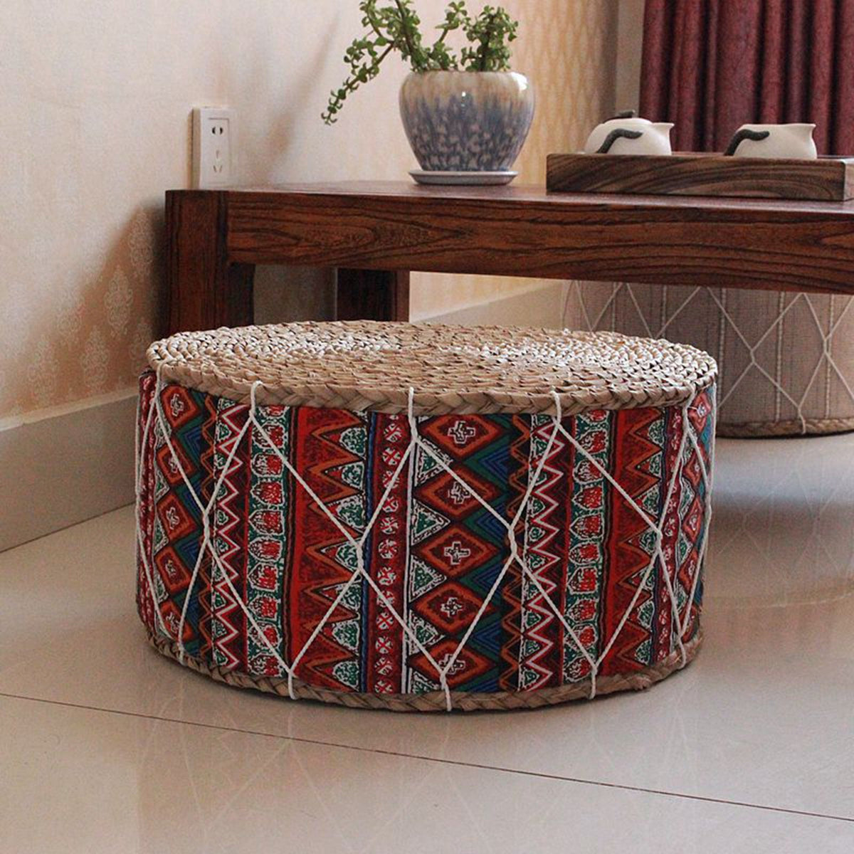 Rattan pouf with burgundy and blue geometric fabric – shown in a room setting