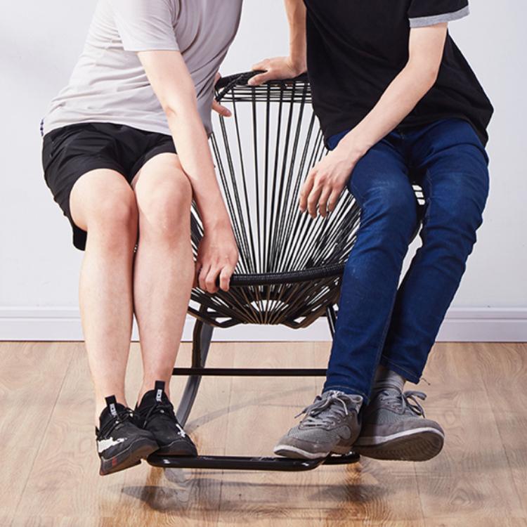 Modern black rattan rocking chair with a hand-braided seat – shown in use