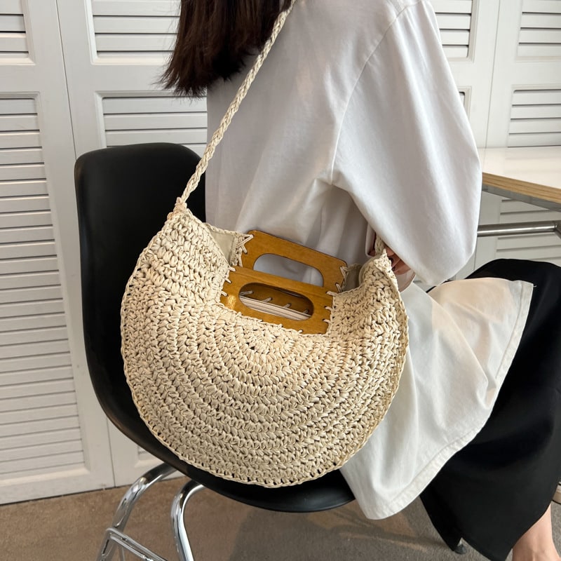 Rounded rattan handbag with a raw wood handle – beige variant, worn by a model