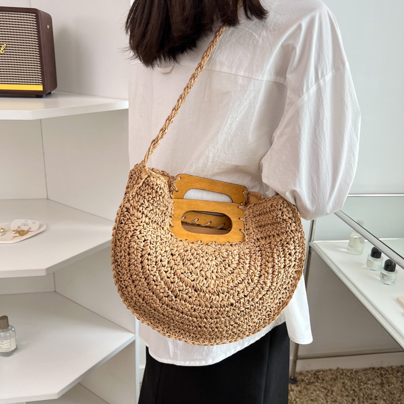 Rounded rattan handbag with a raw wood handle – brown variant, worn by a model