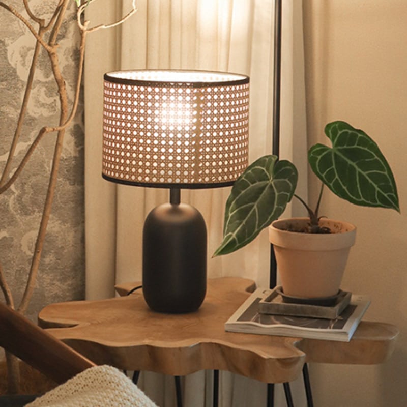 Rattan LED desk lamp with a handwoven shade and black metal base – shown in a room setting