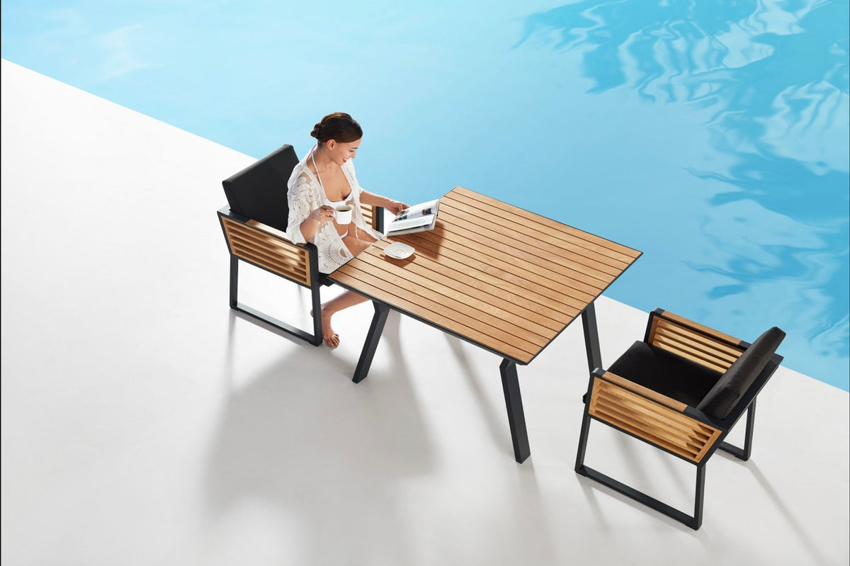 Cofy teak slat outdoor dining armchair with black aluminum legs – shown outdoors