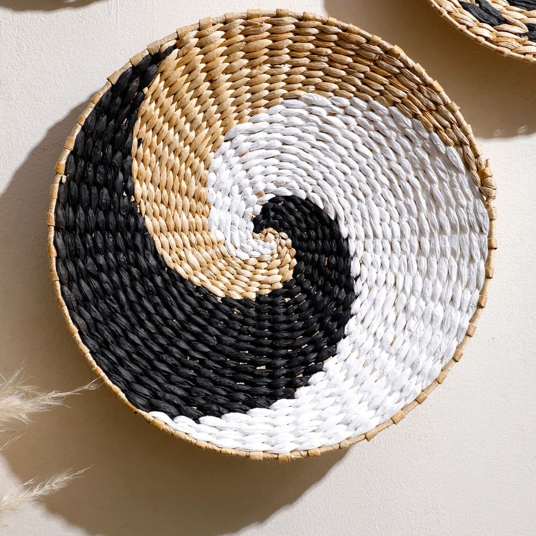 Round rattan wall hanging trimmed with ecru cotton pom-poms – shown in a room setting