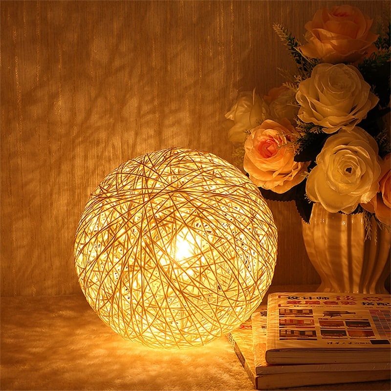 Hand-braided rattan ball LED bedside lamp – shown lit in a room setting (2)