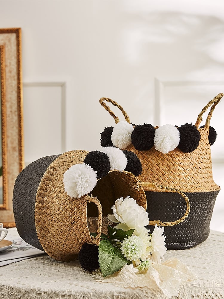 Black rattan basket with braided handles and black-and-white pompoms – shown in a room setting