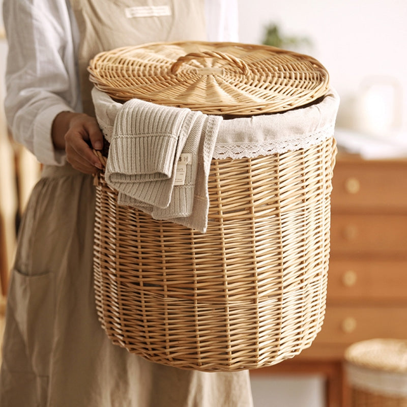 Hand-braided rattan laundry basket with a removable lid and handles – shown in a room setting