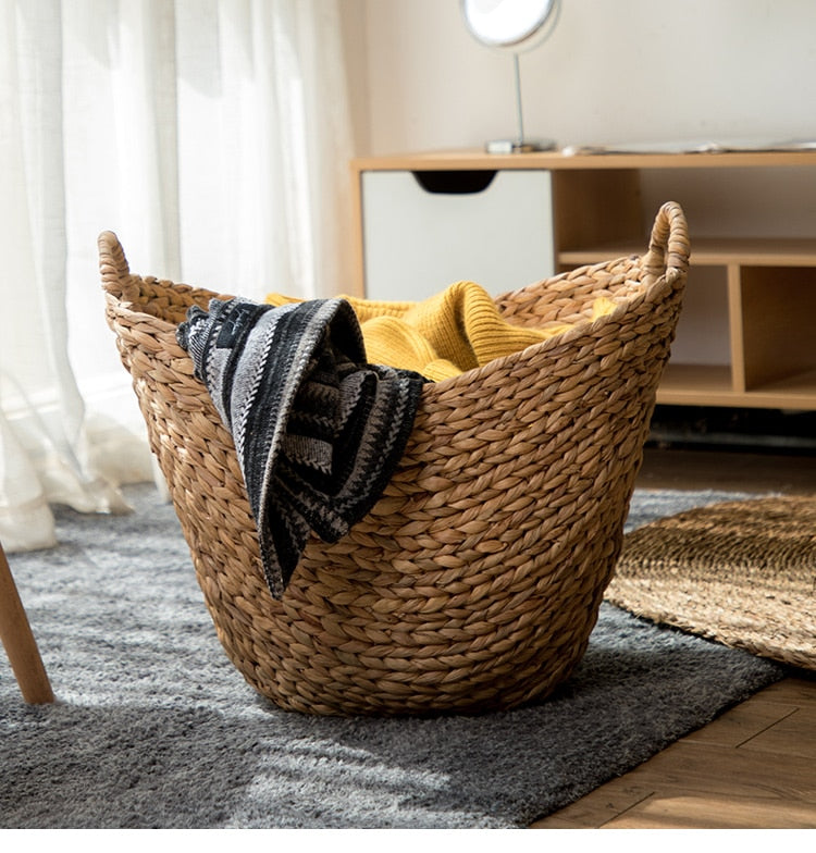 Natural rattan laundry basket with two side handles – shown in a room setting
