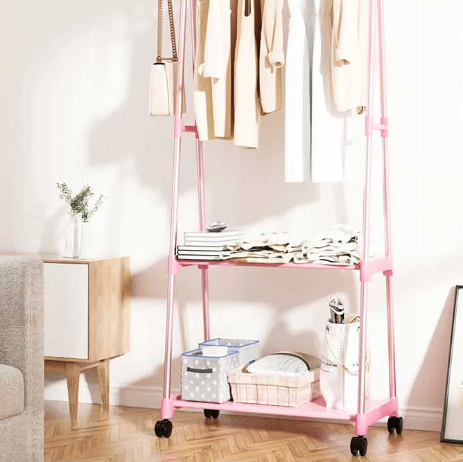 Pink two-tier rolling clothing rack with wood-look uprights – shown in a room setting