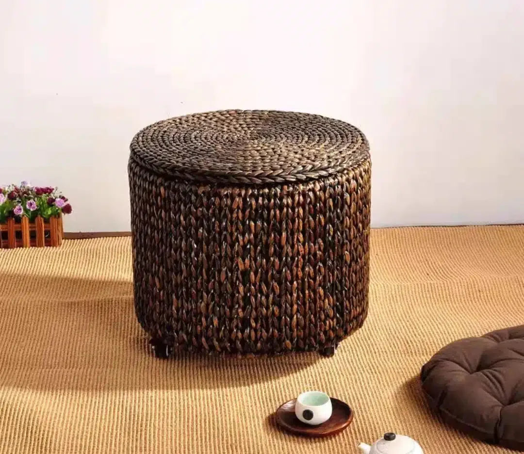 Brown hand-braided rattan footstool on casters with a removable lid – shown in a room setting (2)